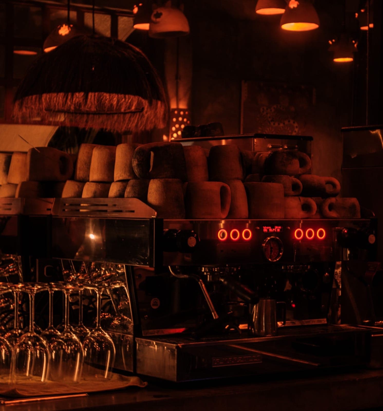 The bar by lamplight, cups stacked on the espresso machine