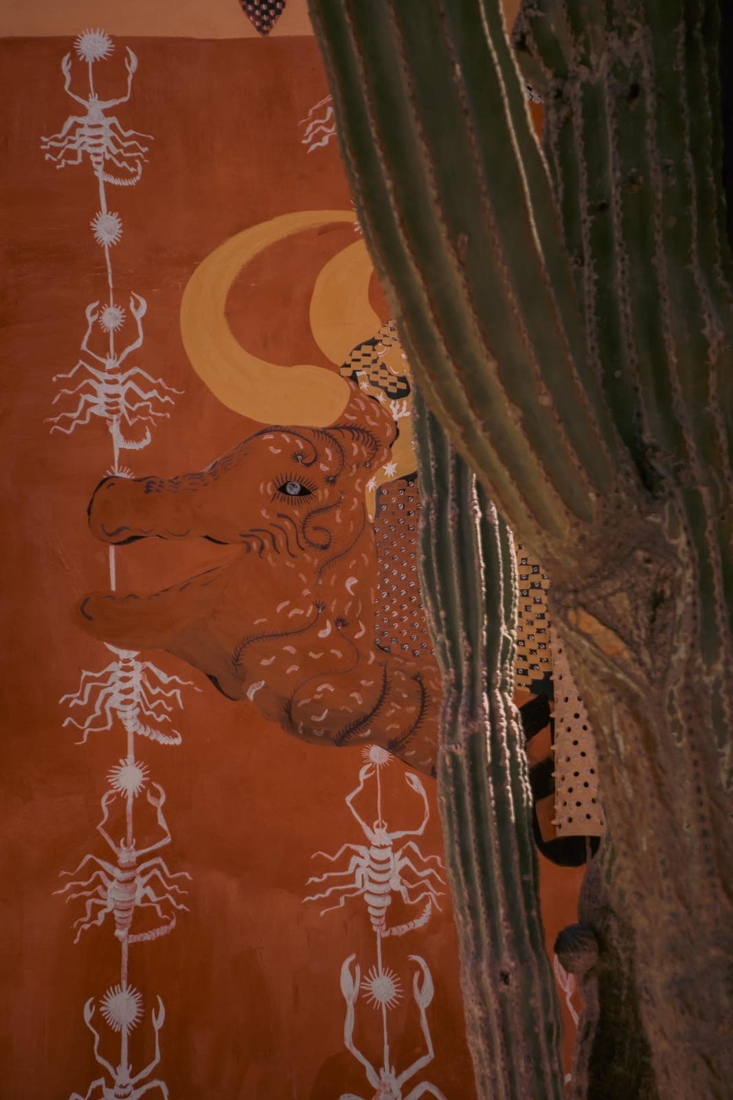 A mural of a bull and scorpions behind a cardón