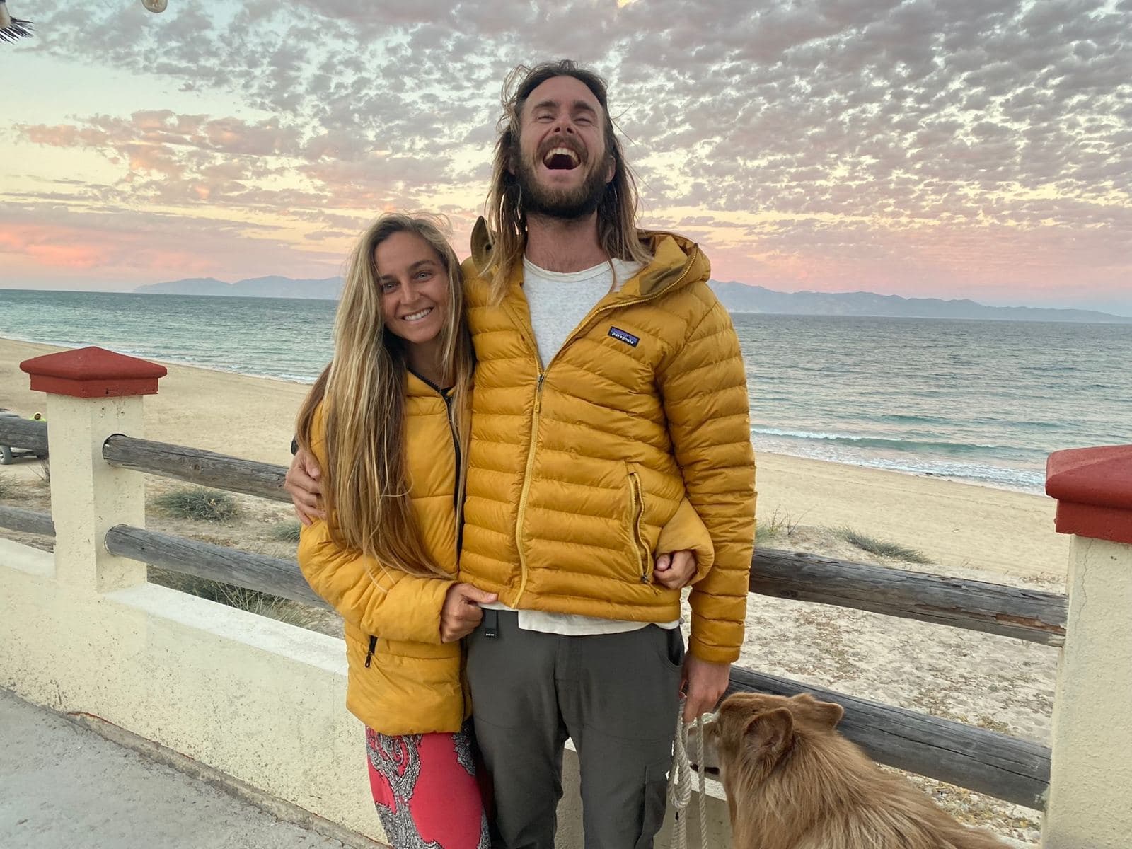 Cody and Falyn on a sea wall at sunset, Captain at their feet